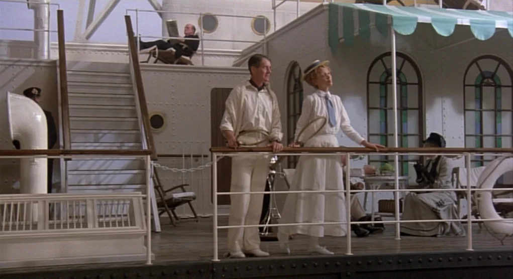 Time Bandits (1981) movie still: wide — The metal deck of a luxury ocean liner features white steel railings and stairs. A man and a woman in tennis…