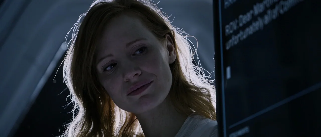 The Martian (2015) movie still: closeup — A dimly lit interior space with a dark, metallic environment. A woman views text on a vertical glowing…