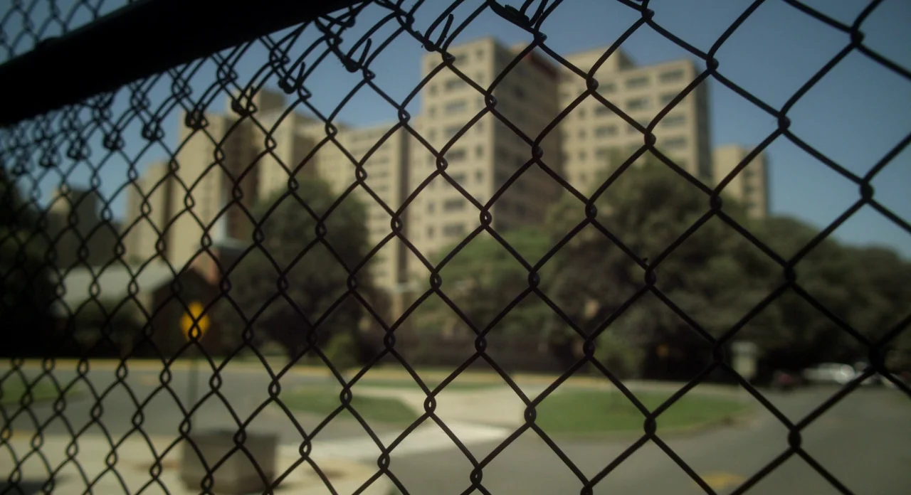 Side Effects (2013) movie still: establishing — A tall, tan-colored multi-story concrete building sits in the background of a landscaped area. A…