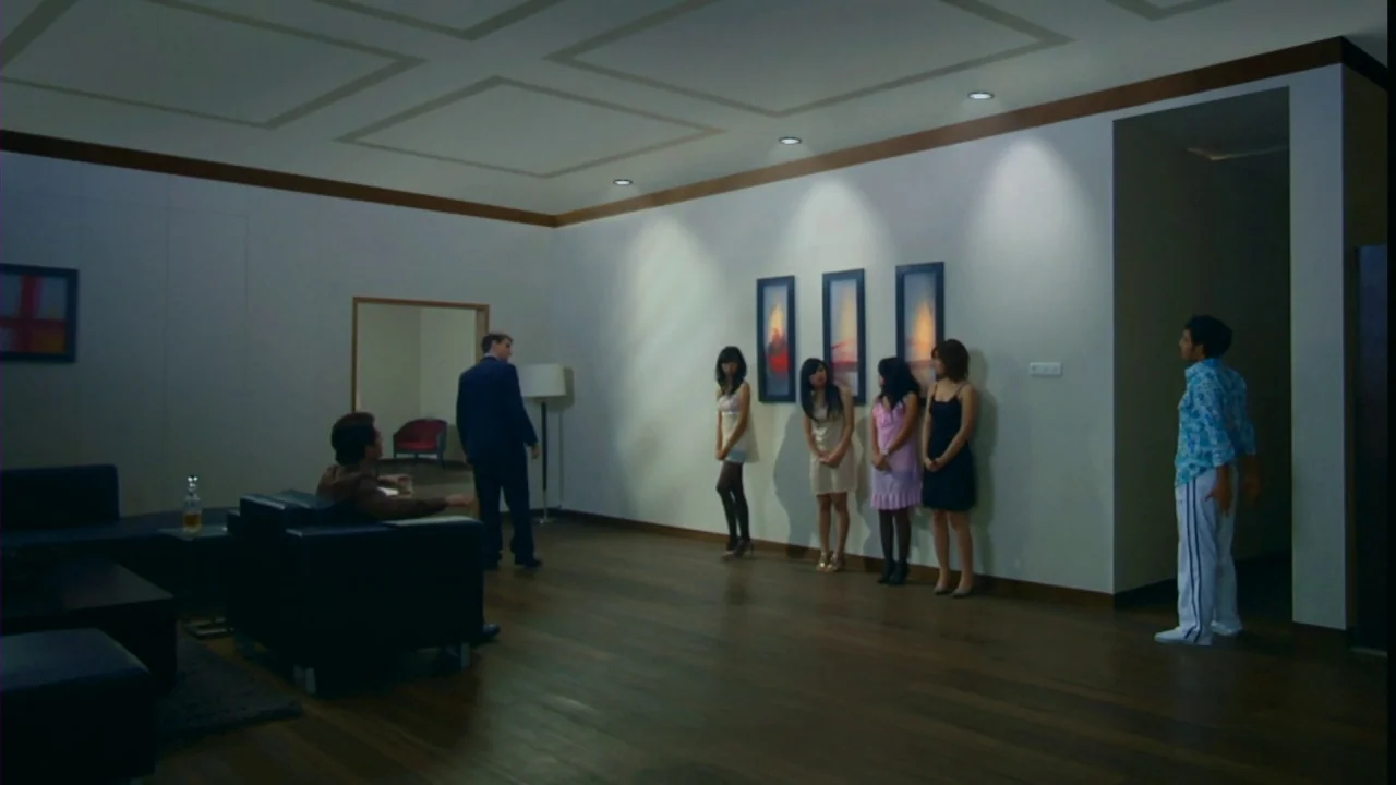 Merantau (2009) movie still: wide — A spacious room features hardwood floors and three framed paintings on a white wall. Six people are scattered…