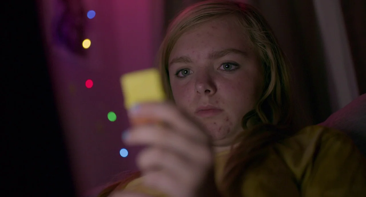 Eighth Grade (2018) movie still: closeup — A dark, dimly lit indoor space with decorative fairy lights blurred in the background. A teenage girl…