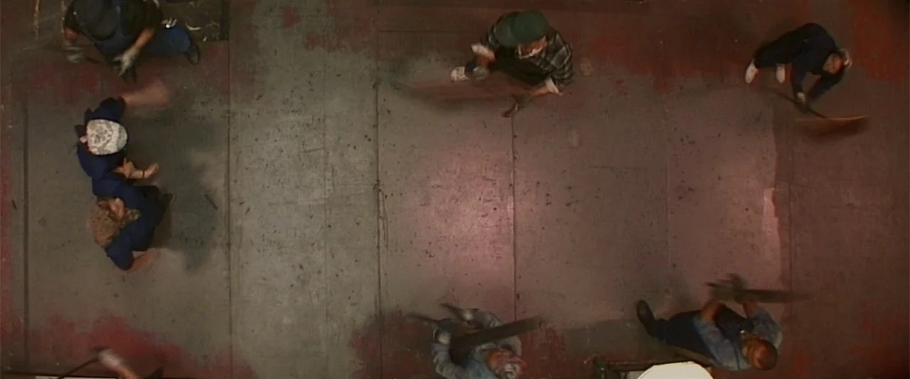 Dancer in the Dark (2000) movie still: wide — A concrete floor marked with patches of red paint fills the frame from above. Five people in work…