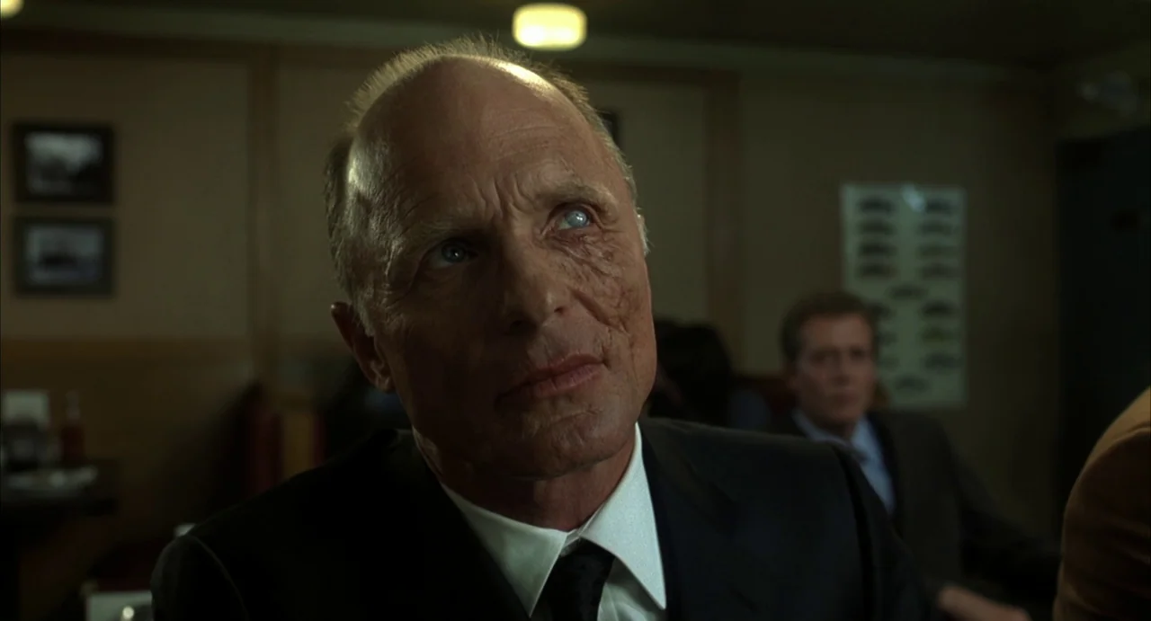 A History of Violence (2005) movie still: closeup — A dimly lit diner with dark wood-paneled walls and muted interior decor. An elderly man with a…