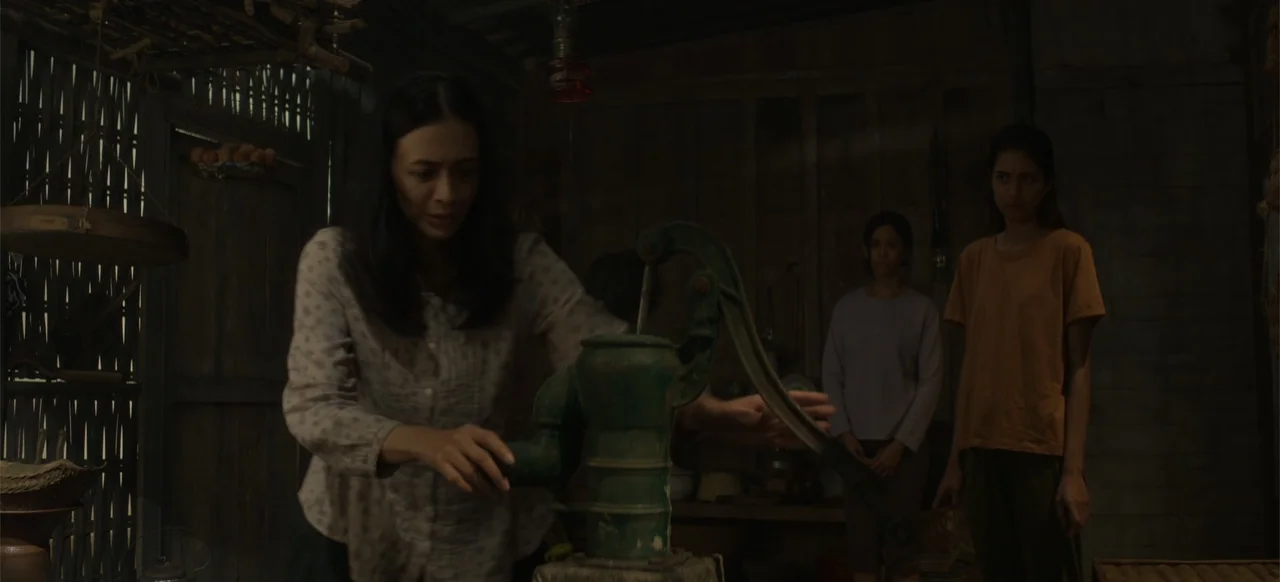 A Thousand Days (2023) movie still: medium — A dimly lit room features walls constructed from vertical wooden planks and woven bamboo panels. A…