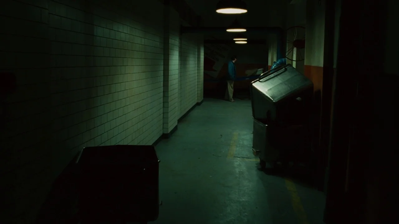 Saw III (2006) movie still: wide — A long, dark concrete hallway features tiled walls and multiple overhead industrial light fixtures. A lone man in…