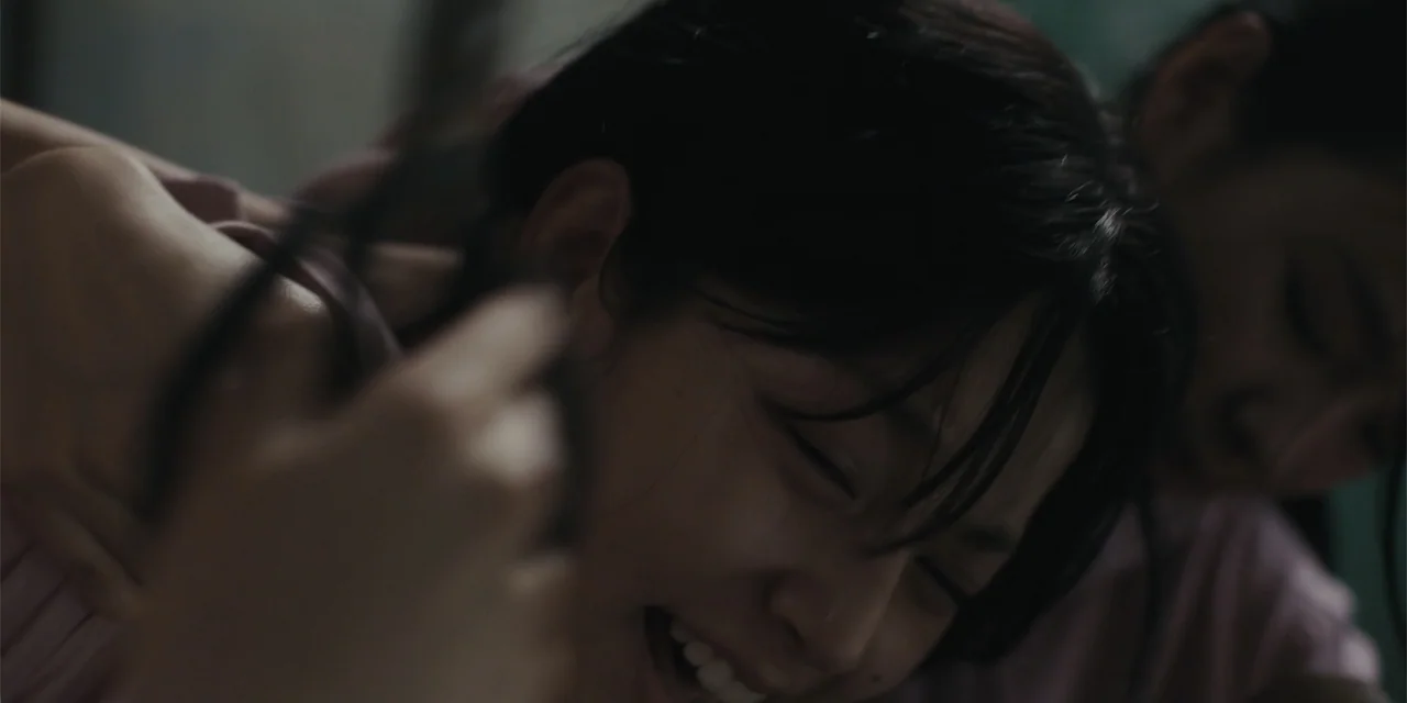 Host (2020) movie still: closeup — An interior space with low light levels and muted colors. A woman with dark hair grimaces with her eyes closed.