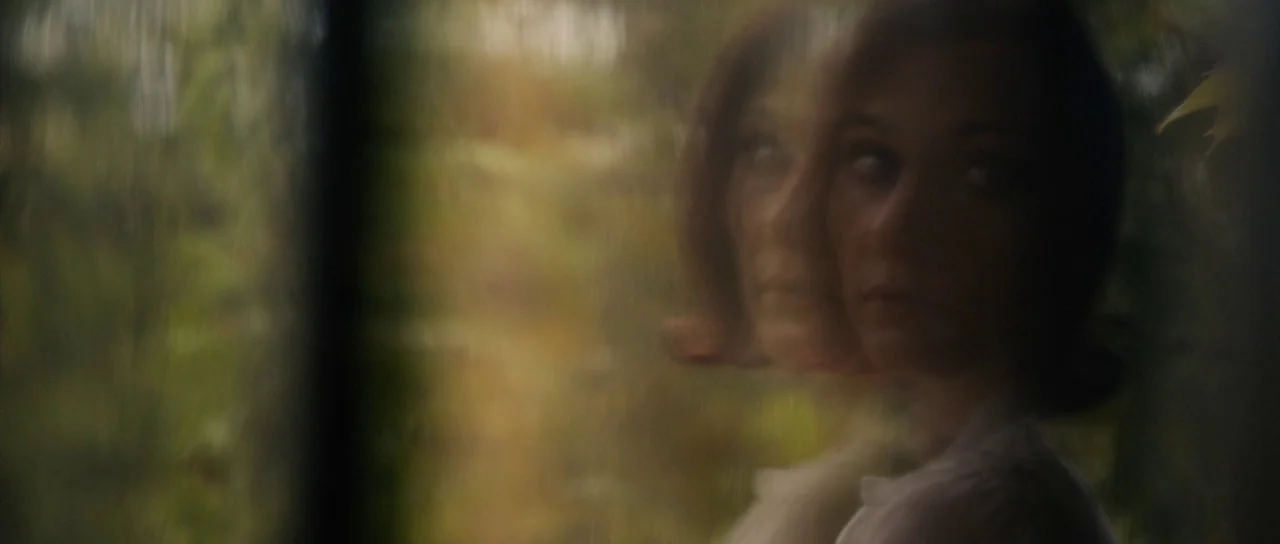 The Duke of Burgundy (2014) movie still: closeup — A woman is framed through a double-exposed glass refraction effect against a blurred woodland.…