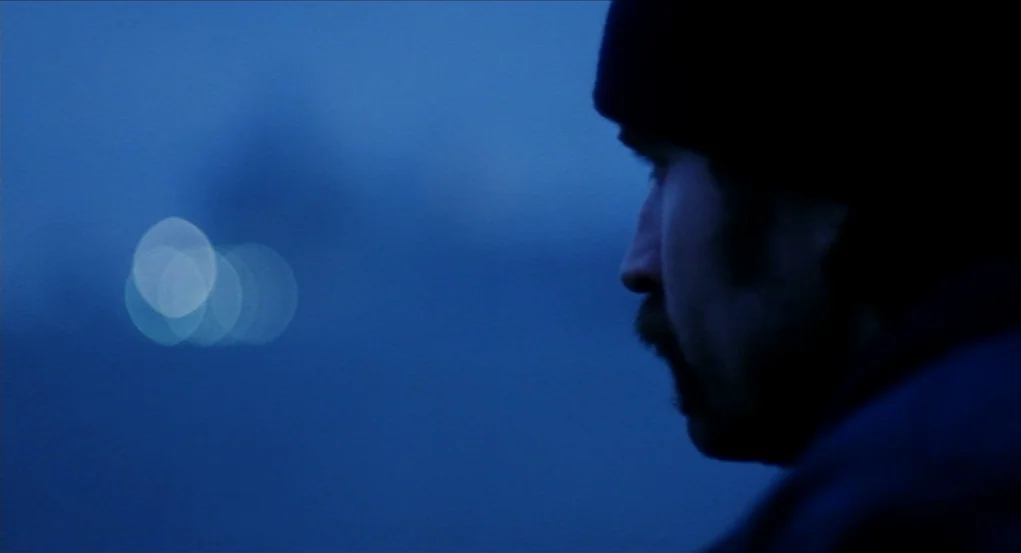 Narc (2002) movie still: closeup — A dark urban environment at night with blurred bokeh lights in the distance. A man in a dark jacket and beanie…