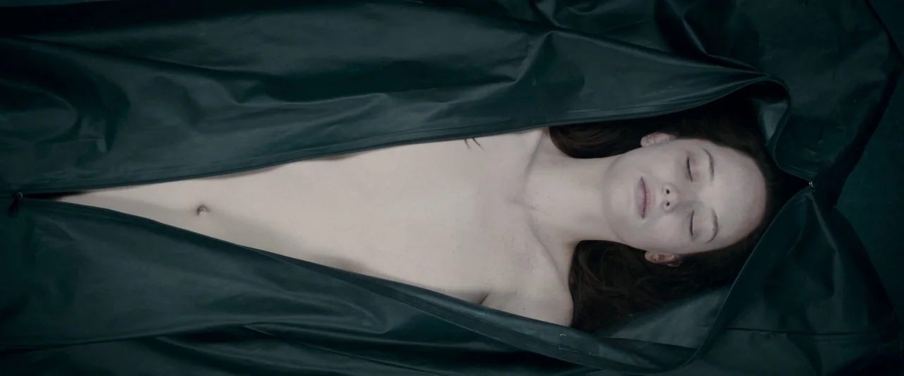 The Autopsy of Jane Doe (2016) movie still: medium — A dark, rubberized body bag is partially unzipped to reveal a woman's torso and face. The woman…