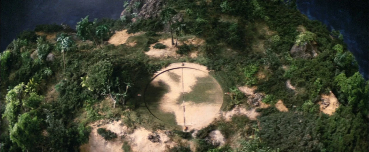Destroy All Monsters (1968) movie still: establishing — A dense jungle covers an island terrain surrounding a circular concrete helipad or landing…