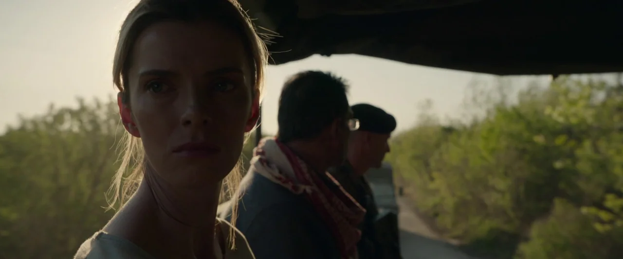 The Hunt (2020) movie still: closeup — A woman sits in an open-air vehicle with trees visible in the background. Two men sit behind her while they…