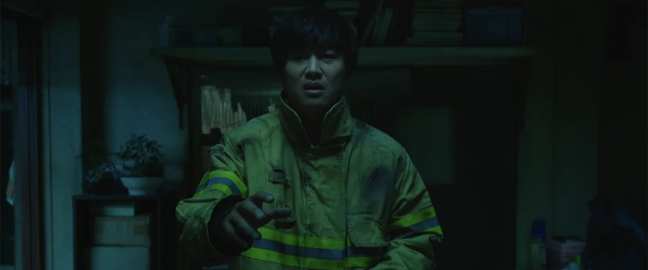 Along with the Gods: The Two Worlds (2017) movie still: medium — A dimly lit indoor space features a dark, cluttered background with soft focus…