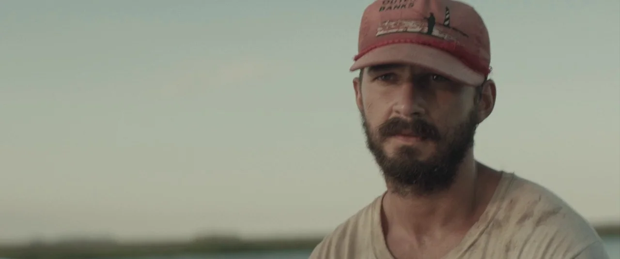 The Peanut Butter Falcon (2019) movie still: closeup — An open water setting with a blurred shoreline visible in the soft-focus background. A man…
