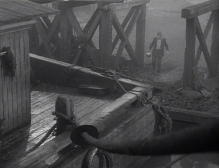 Anna Christie (1930) movie still: wide — A foggy, dark wooden pier with heavy timber supports and roped moorings. A man walks away from the…
