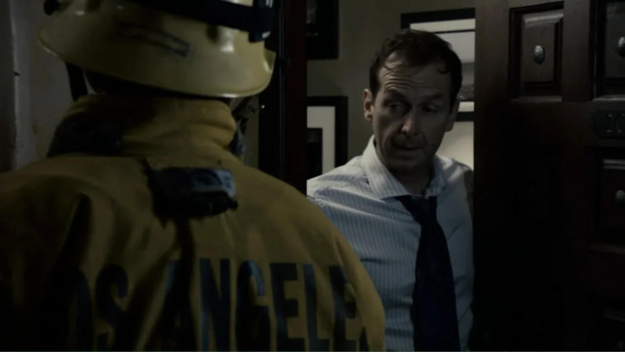 Quarantine (2008) movie still: medium — A dark hotel hallway interior featuring a door frame and wood-paneled wall. A man in a business shirt stands…