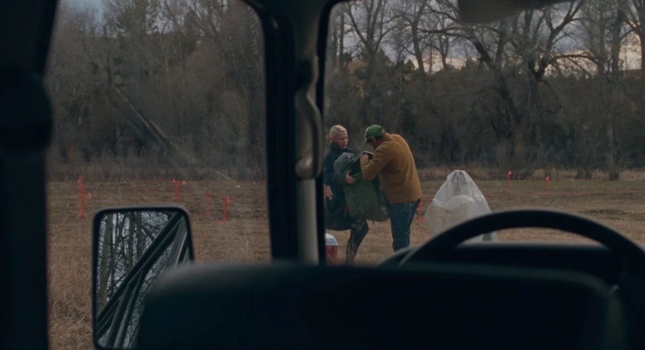 Certain Women (2016) movie still: wide — An open field with sparse winter trees and small red survey flags in the ground. A man and woman stand…
