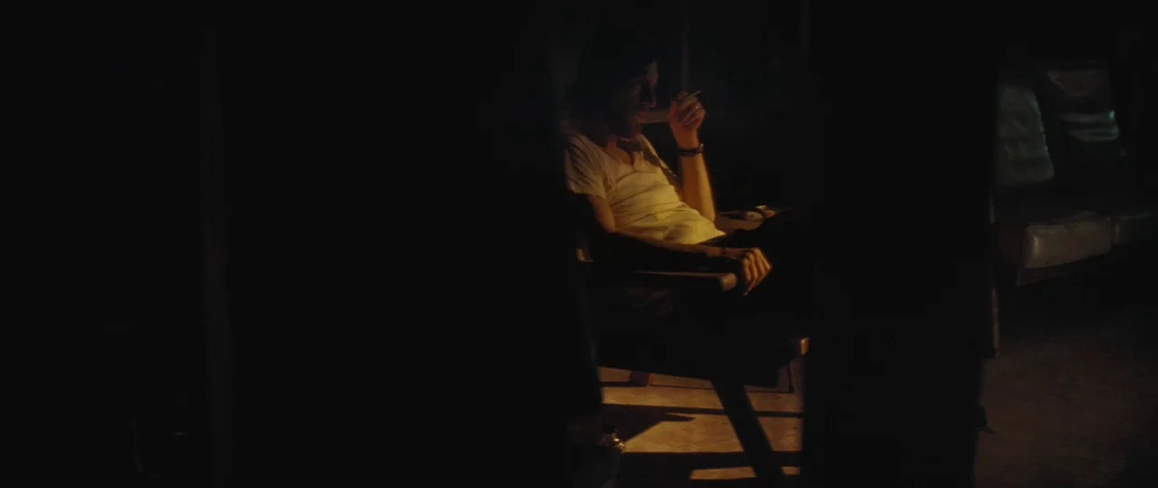 Mud (2012) movie still: medium — A man sits in a dimly lit room with only a warm light source. He rests in a chair while holding a cigarette in his…