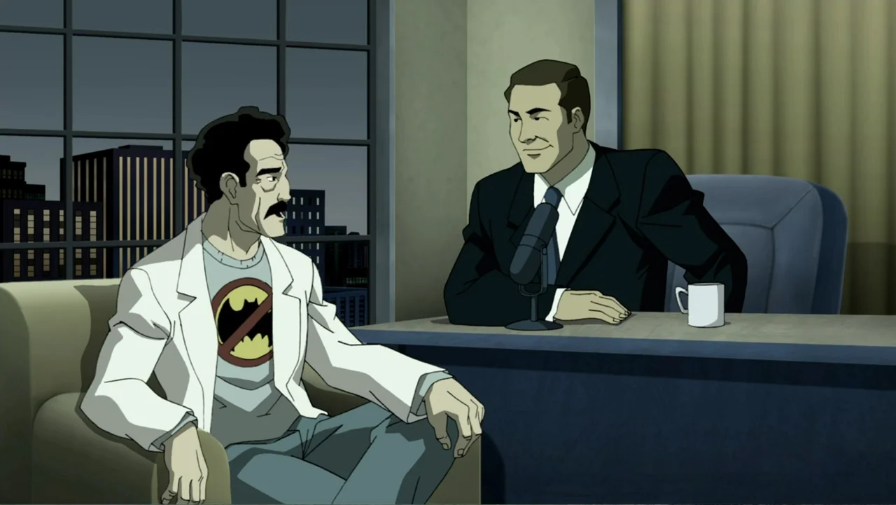 Batman: The Dark Knight Returns, Part 1 (2012) movie still: medium — A television studio set features a desk and two chairs against a window…