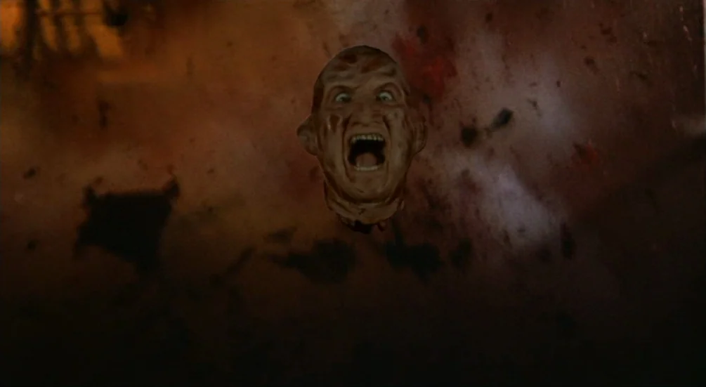 Freddy’s Dead: The Final Nightmare (1991) movie still: closeup — A severed head floats amidst dark, swirling smoke and debris against a black…