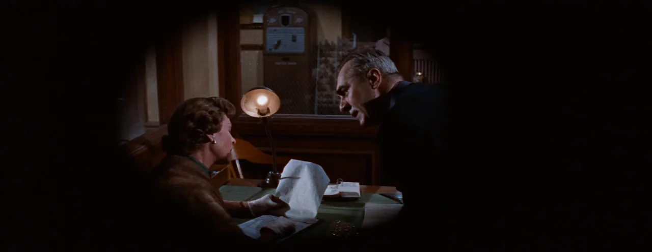 Rebel Without A Cause (1955) movie still: medium — A dimly lit room features a wooden desk with a single illuminated lamp fixture. A man in a dark…