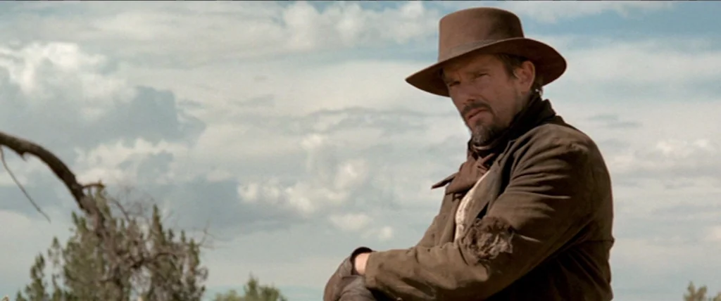 In A Valley of Violence (2016) movie still: medium — A man stands in an open wilderness area with a distant horizon under a sky. The man is wearing…