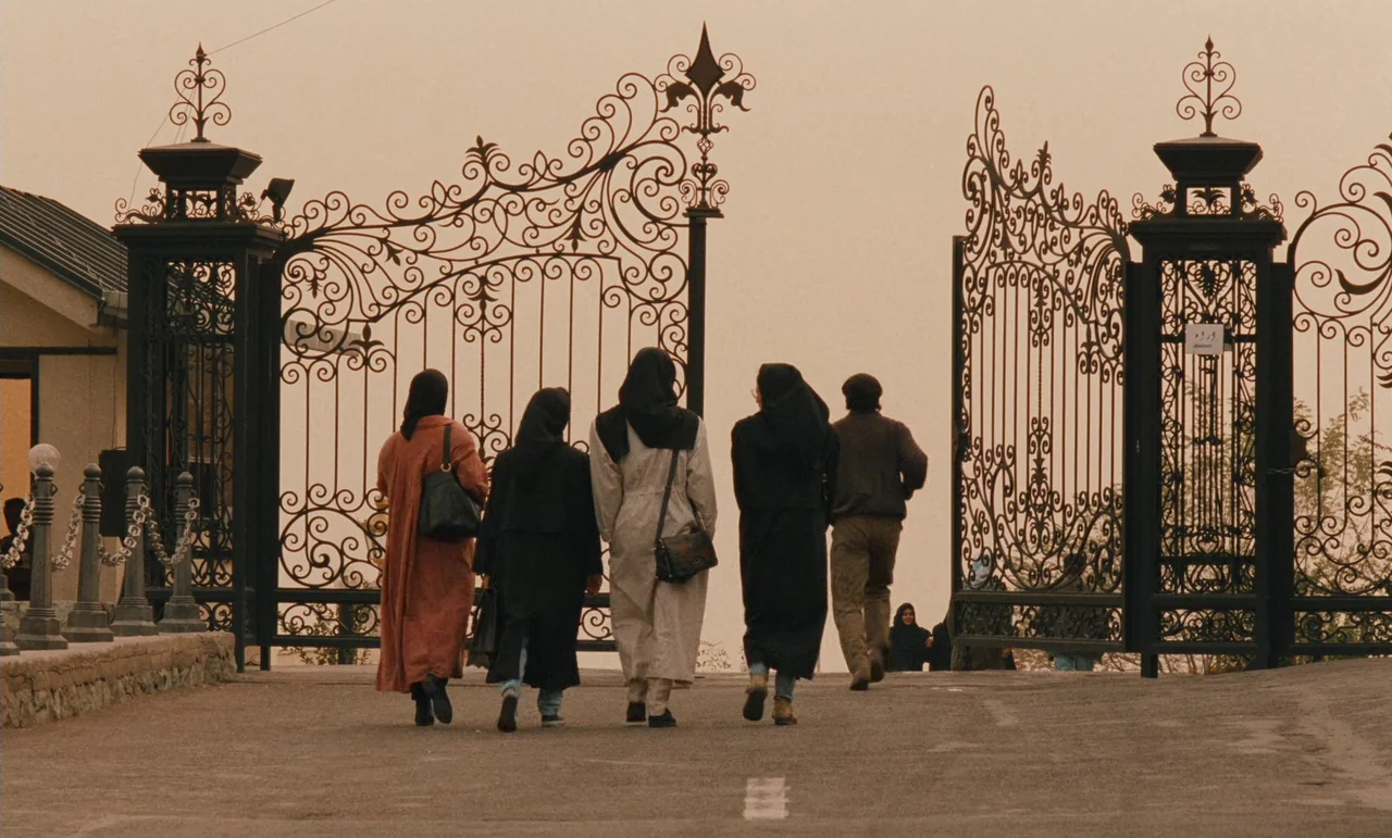 Taste of Cherry (1997) movie still: fullbody — An asphalt road leads toward a large, intricate wrought-iron gate set in a wall. Five individuals…