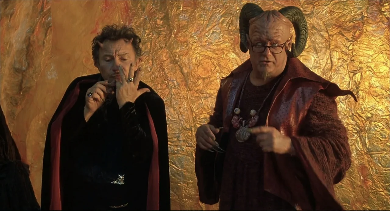 Little Nicky (2000) movie still: medium — Two individuals with horn-like prosthetics stand against a crumpled gold-foil background. They appear to…
