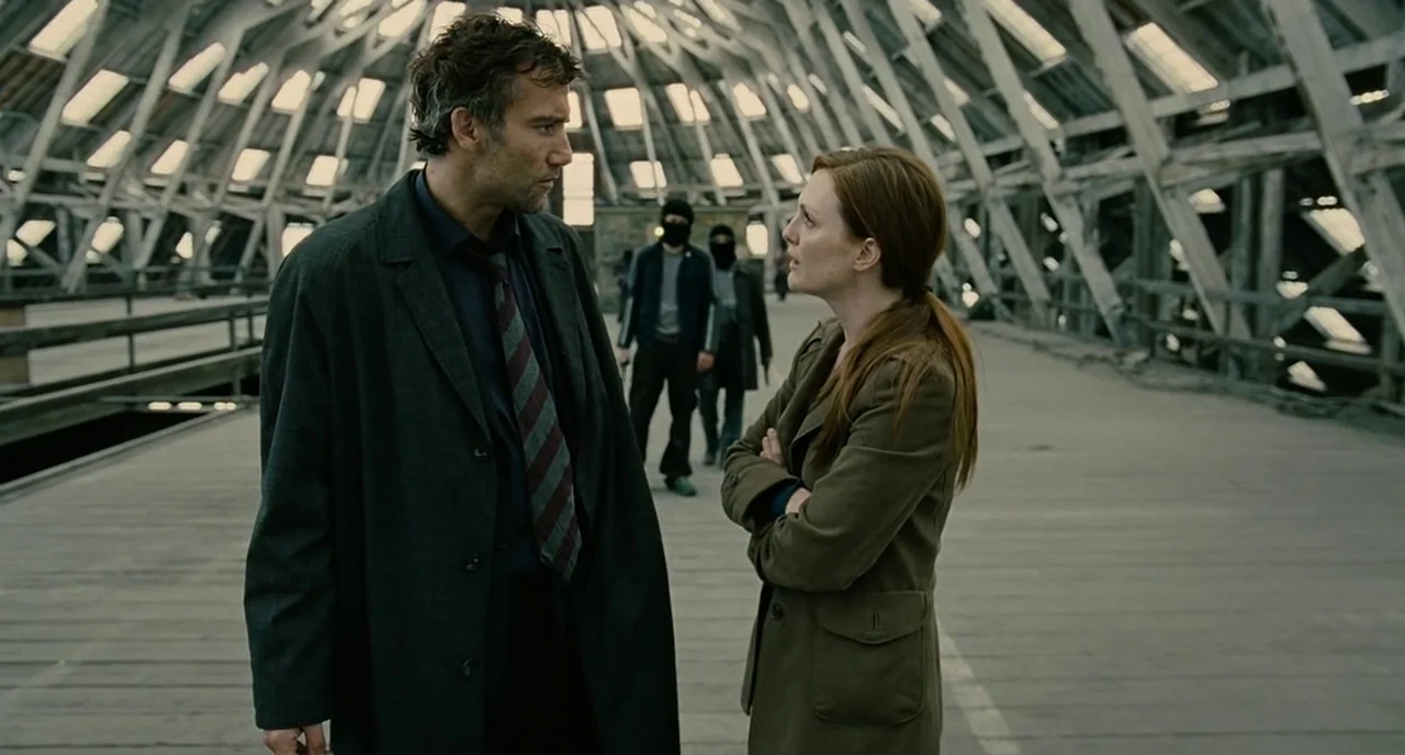 Children Of Men (2006) movie still: medium — A vast attic space with exposed wooden beams and glass panels in the ceiling. A man and a woman stand…