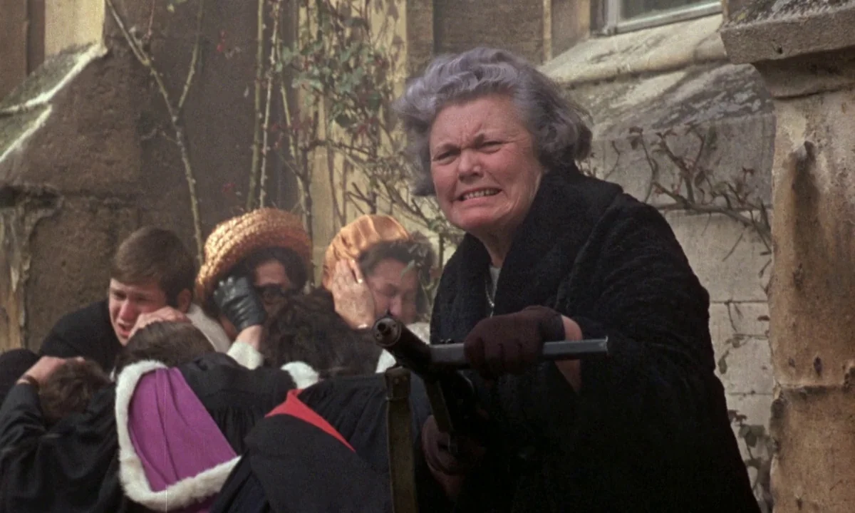 If…. (1968) movie still: medium — An older woman in a heavy coat stands before a weathered stone exterior wall. She grips a submachine gun while…