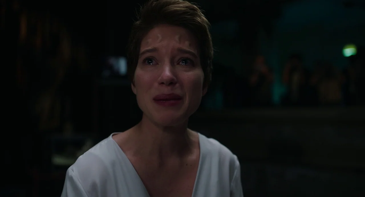Crimes of the Future (2022) movie still: closeup — A dimly lit, dark space serves as the setting for the subject. A woman with short hair cries as…