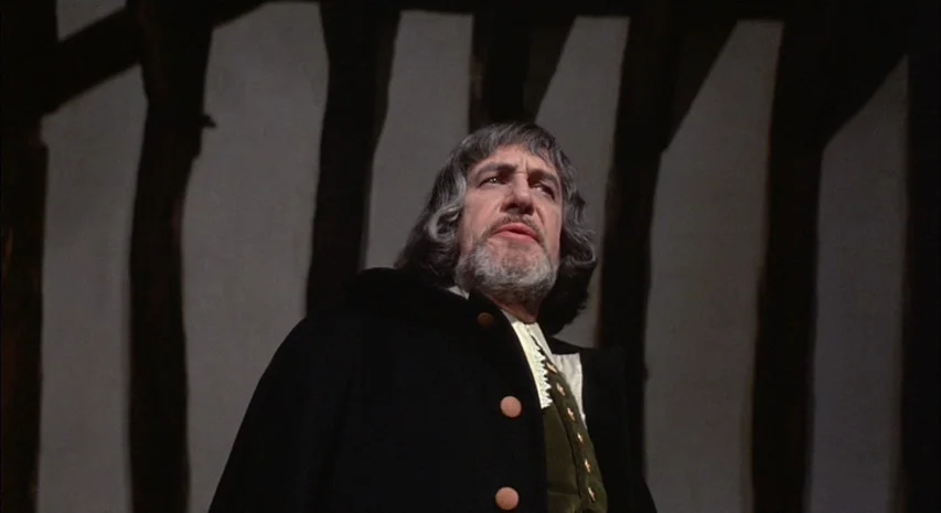 Witchfinder General (1968) movie still: medium — A man stands in an interior space with vertical wooden structural beams in the background. The man…