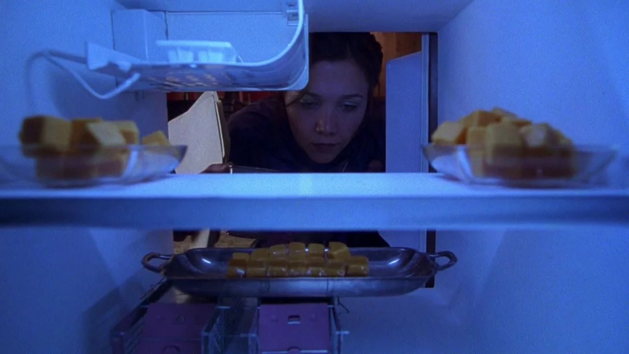 Secretary movie still: medium — A view from inside a refrigerator looking out toward a woman standing in darkness. She gazes into the illuminated…