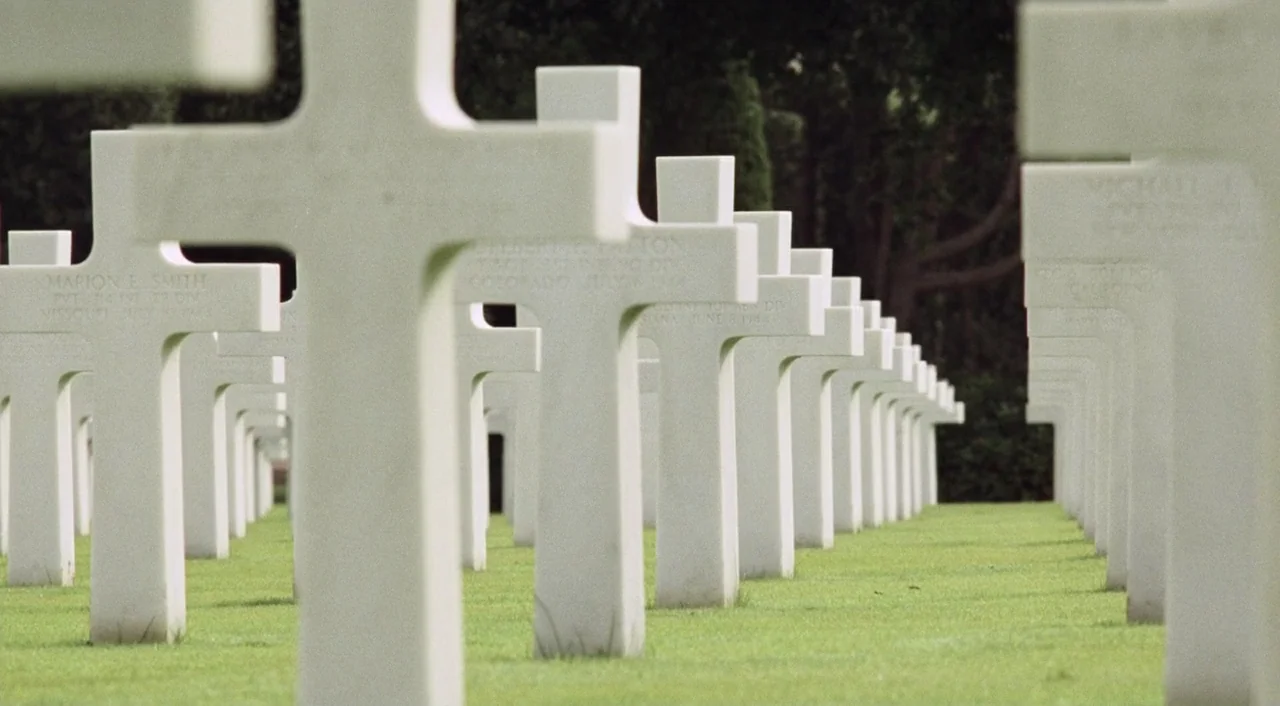 Saving Private Ryan (1998) movie still: wide — Numerous white marble cross headstones stand in perfect rows across a flat green lawn. The markers…