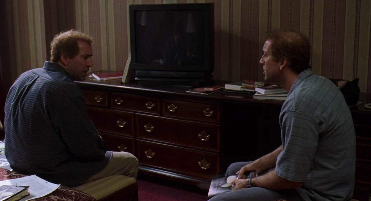 Adaptation (2002) movie still: medium — Two identical men sit facing one another in a hotel room with striped wallpaper. A large dark wooden dresser…
