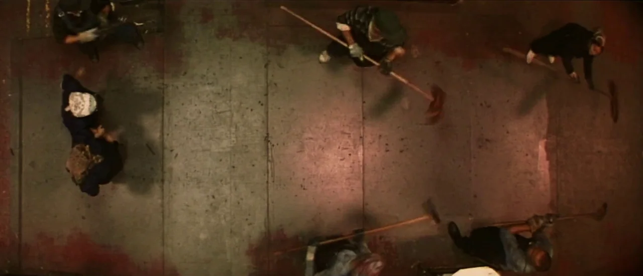 Dancer in the Dark (2000) movie still: establishing — A dark, paved ground is framed from directly overhead in a high-angle shot. Six figures…