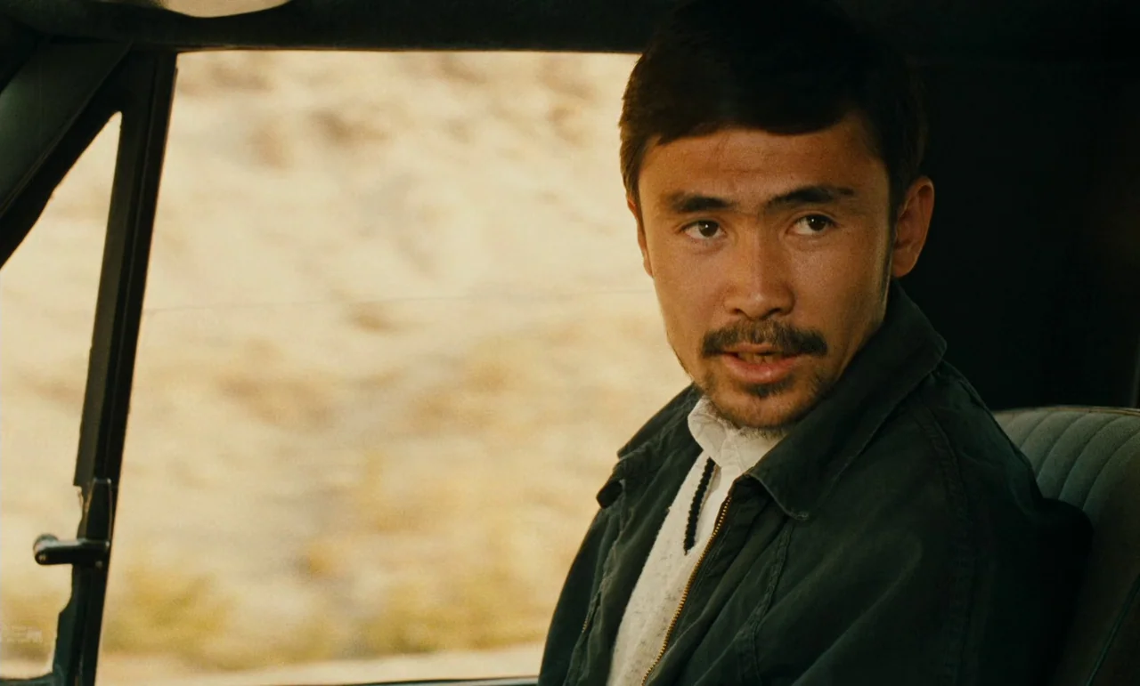 Taste of Cherry (1997) movie still: closeup — A man sits in the driver seat of a vehicle with a desert landscape visible. He turns his head to look…