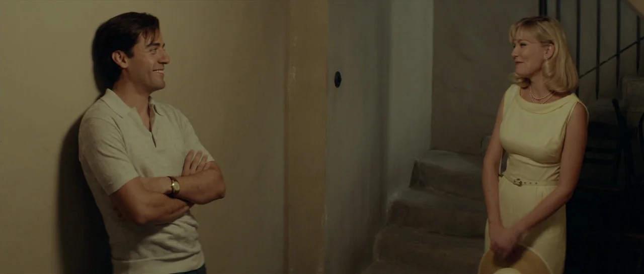 The Two Faces of January (2014) movie still: fullbody — A dimly lit interior stairwell features plain walls and simple concrete stairs. A man leans…