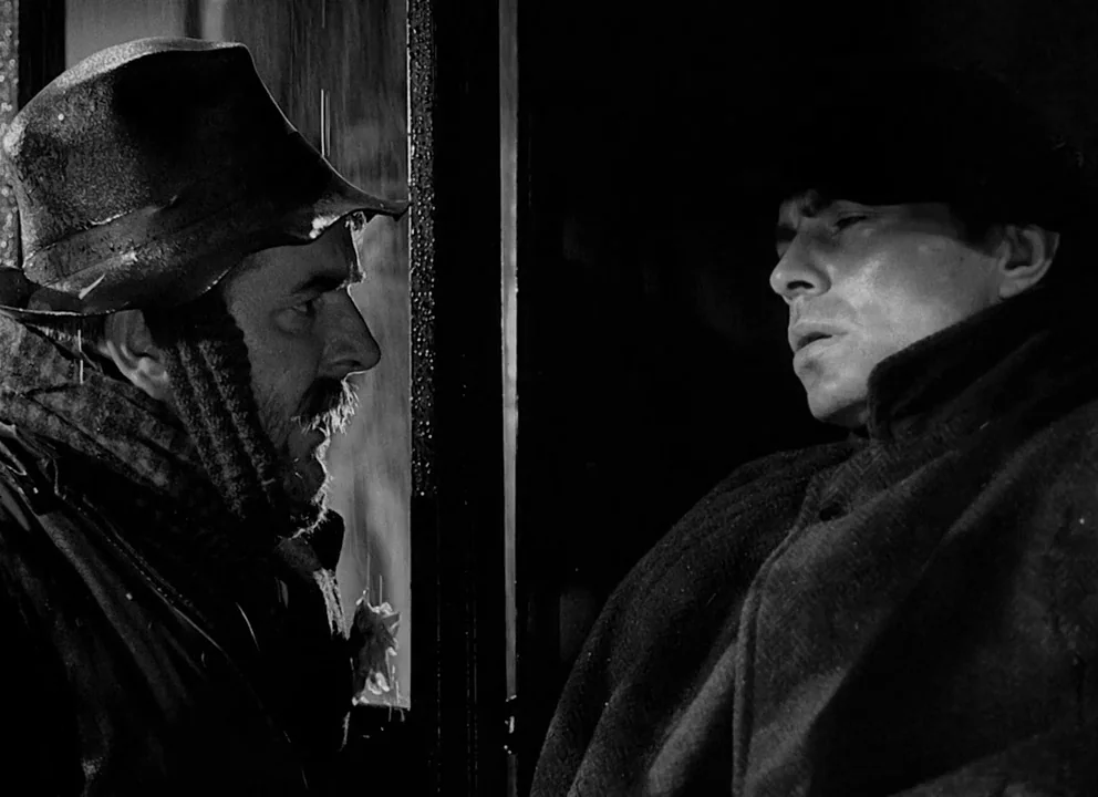 Odd Man Out (1947) movie still: medium — A rain-slicked exterior carriage setting during the night with dark, heavy shadows. Two men in dark coats…