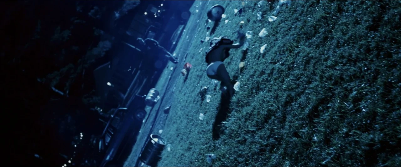 dutch angle shots example from Black Snake Moan: A night exterior showing a suburban lawn strewn with plastic cups and trash. A woman in minimal cloth