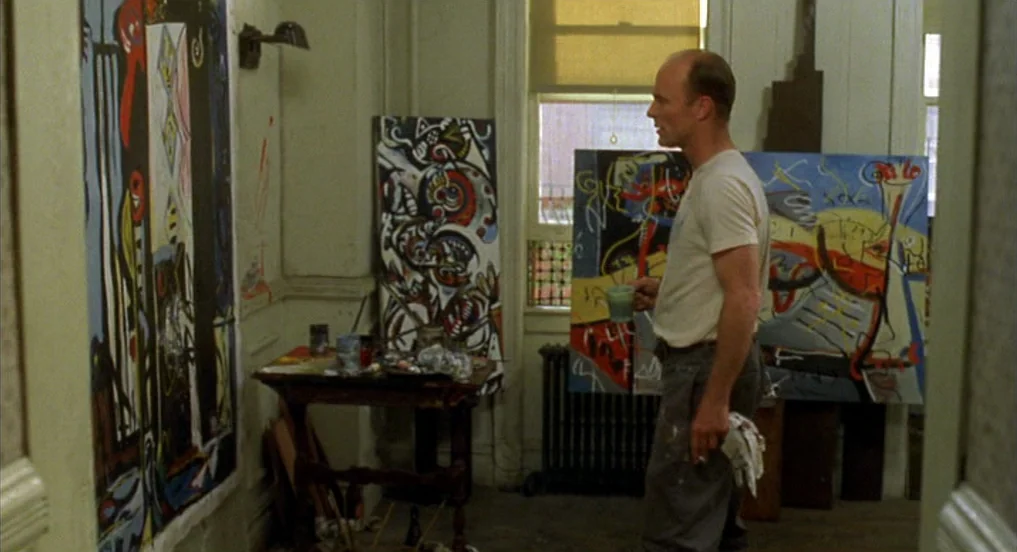 Pollock (2000) movie still: medium — An artist studio contains multiple large, vibrant abstract paintings leaned against the walls. A bald man…