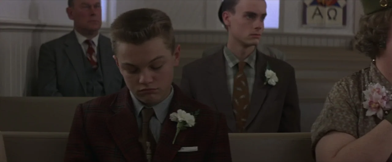 This Boy's Life (1993) movie still: medium — People sit in wooden church pews arranged in rows. A young man in a plaid jacket sits in the foreground.