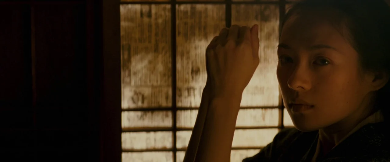 Memoirs of a Geisha (2005) movie still: closeup — A traditional room with a backlit paper lattice window. A young woman stands with her hands raised…
