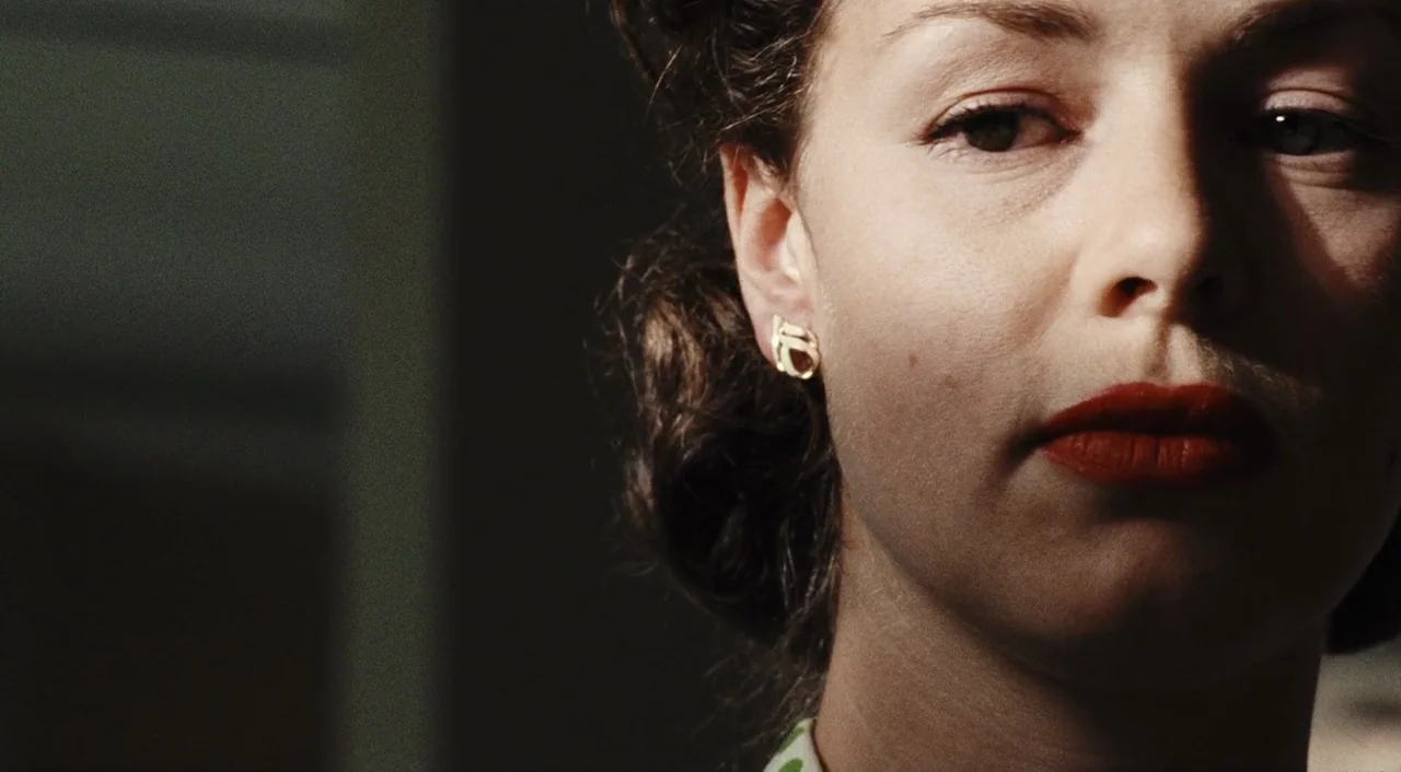 Saving Private Ryan (1998) movie still: closeup — A close-up view shows a woman with dark wavy hair in a shadowed interior. Her face is partially…