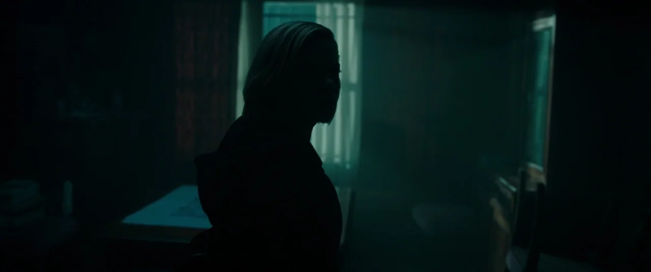 Don’t Breathe (2016) movie still: medium — A dark bedroom illuminated primarily by a backlit window draped with sheer curtains. A woman in a hooded…