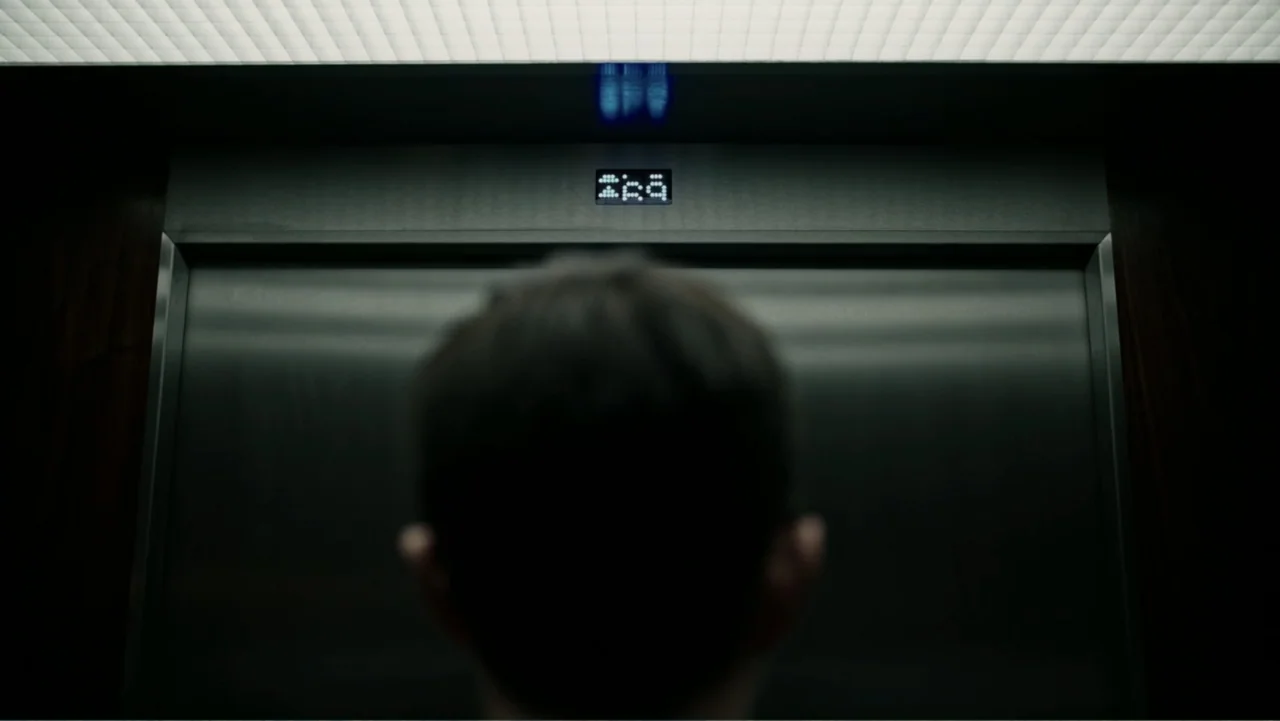 A Cure for Wellness (2017) movie still: medium — A modern elevator interior with brushed metal doors and a glowing digital floor indicator. A man…