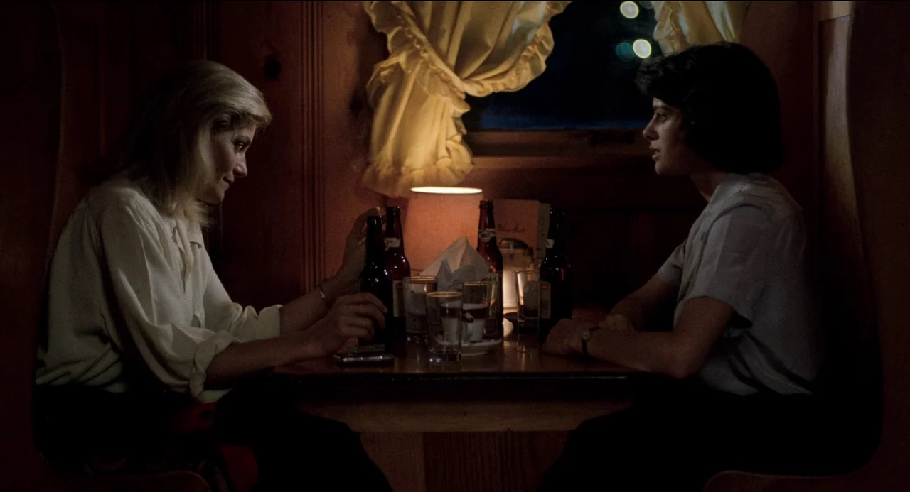 Desert Hearts (1985) movie still: medium — A wood-paneled booth inside a dimly lit restaurant features a single small table lamp. Two women sit…