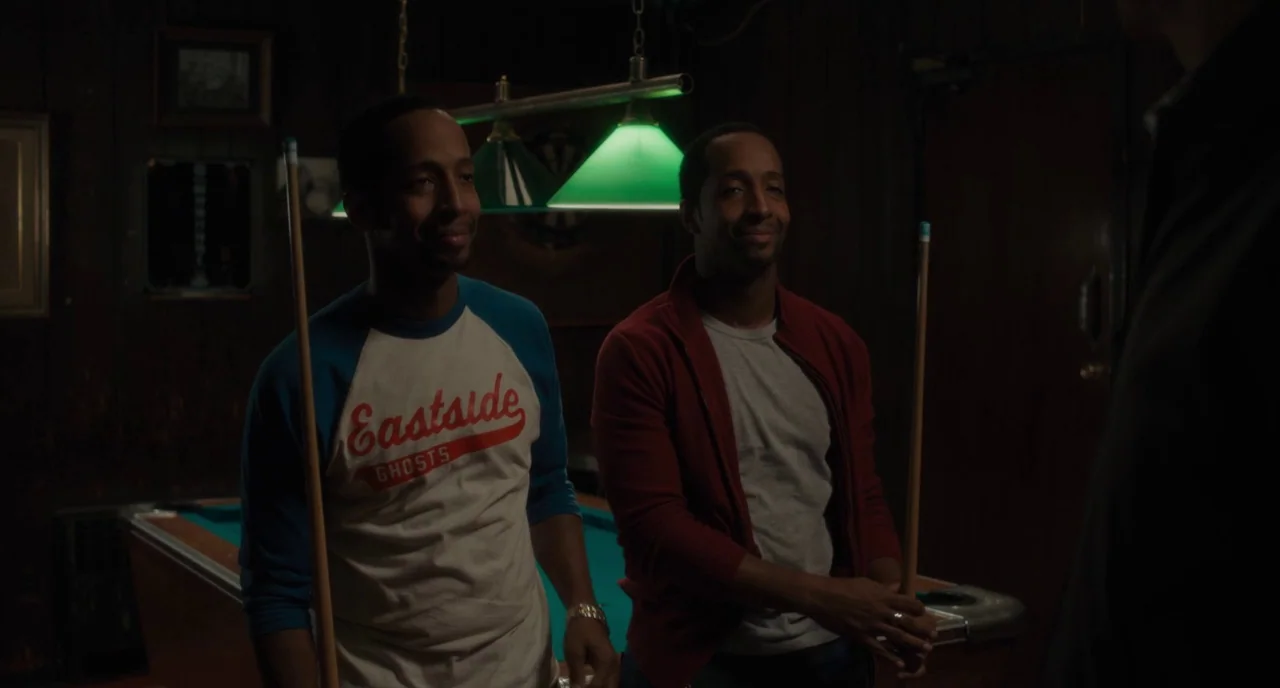 Paterson (2016) movie still: medium — A dimly lit room with wood-paneled walls features a pool table and green lights. Two men wearing casual attire…