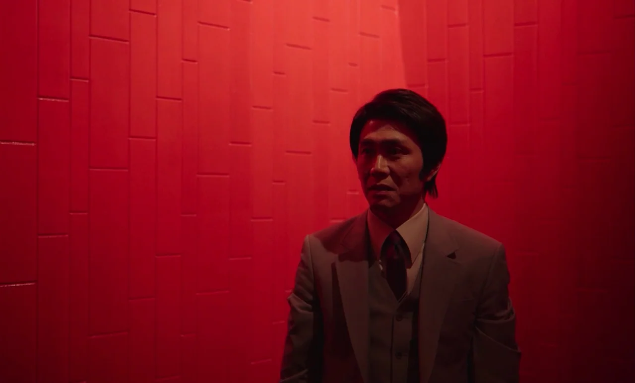 Cobweb (거미집) (2023) movie still: medium — A narrow passage is enclosed by bright red, vertically-aligned wall panels. A man in a light grey suit…