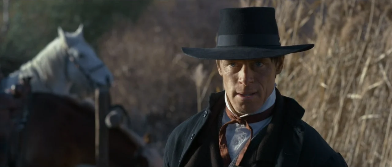 Out of Liberty (2019) movie still: medium — A man in nineteenth-century clothing stands in an open area with tall dry grass. A horse stands blurred…