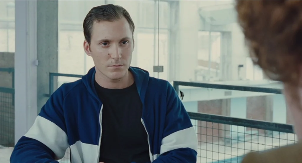 Something in the Air (2012) movie still: medium — An interior space with industrial features and large windows letting in bright daylight. A man in…